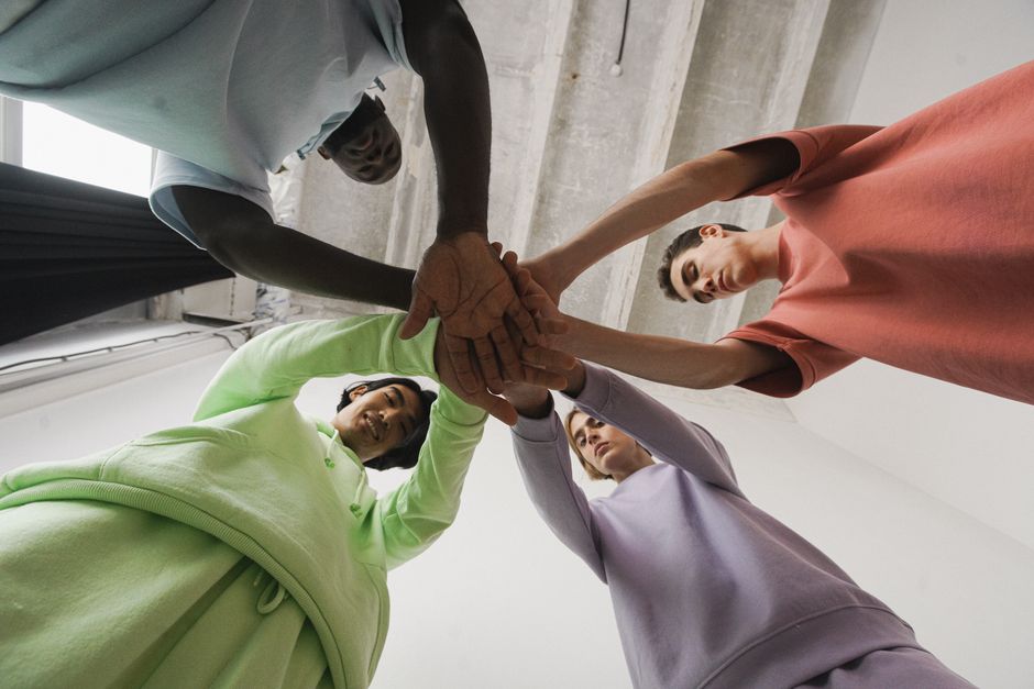 Four diverse individuals in colorful attire join hands symbolizing unity and teamwork in a modern setting.